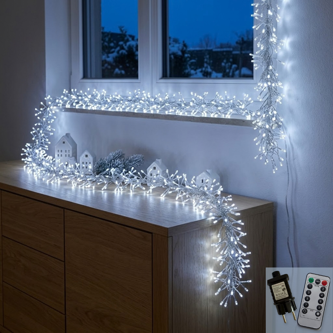 Cluster copper wire LED string lights glowing cool white, draped around a window frame and along the top of a wooden sideboard with small white house ornaments and a frosted pine sprig, with a snowy garden visible through the window at dusk; an inset in the lower right corner shows the plug-in transformer and the numbered remote control.