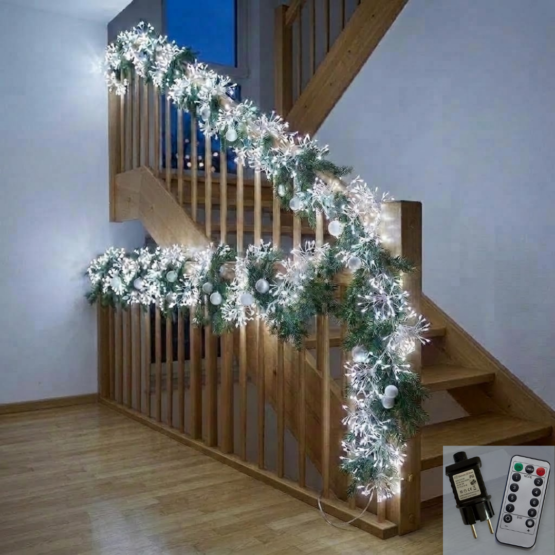 Cluster Copper Wire LED String Lights glowing warm white along a wooden staircase banister, wound through a green pine garland with white snowflake sprays and frosted baubles, with an inset in the corner showing the plug adapter and the white remote control.