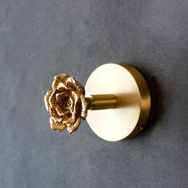 Rose version of the Solid Brass Animal Head Coat Hook mounted on a grey wall, with a round brass backplate, a short cylindrical arm and a sculpted open rose at the end, all in polished gold-toned brass.