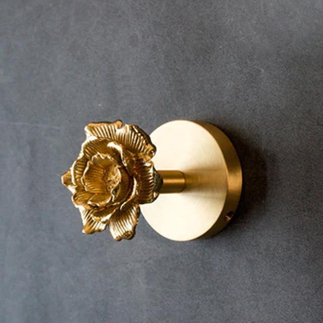 A solid brass coat hook mounted on a grey wall, with a round backplate and a short arm ending in a cast rose-shaped head.