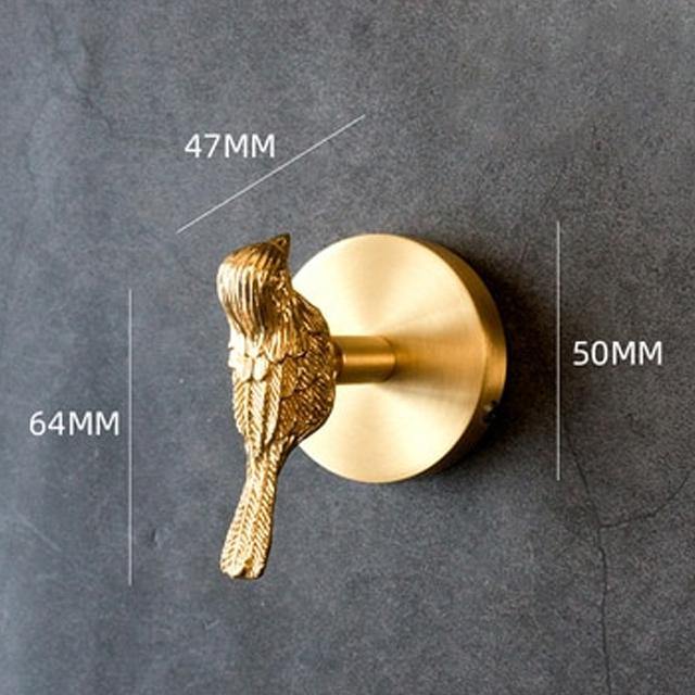 Gold-toned Solid Brass Animal Head Coat Hook shaped like a bird perched on a round wall plate, mounted on a dark grey wall with dimension labels reading 47MM, 50MM and 64MM.