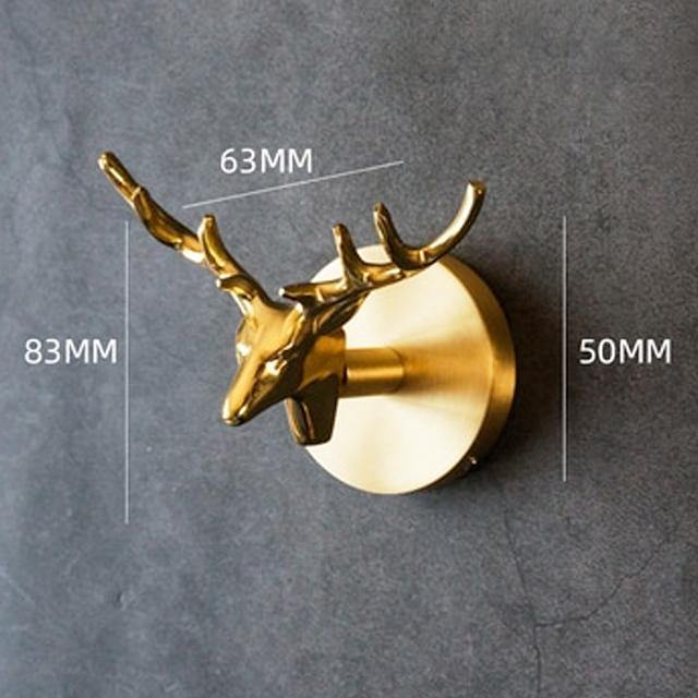 Gold deer head Solid Brass Animal Head Coat Hook mounted on a grey stone wall, with measurement lines marking 63MM across, 83MM high and 50MM deep.