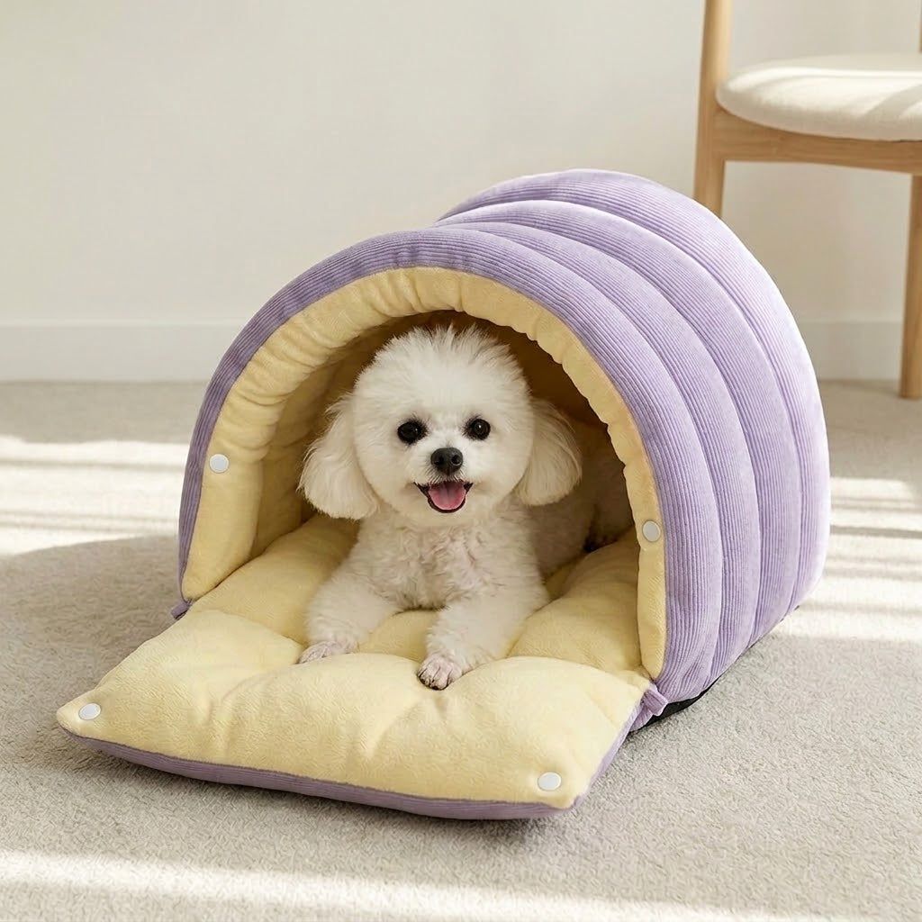 Small white fluffy dog lying inside the lilac Plush-Lined 2-in-1 Cat & Small Dog Cave Bed, with its arched corduroy hood over a yellow plush mat on a pale carpet.
