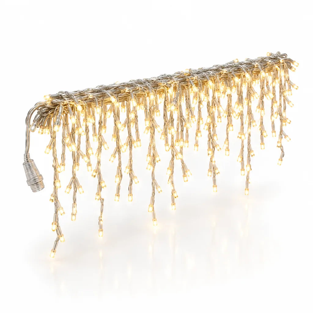 A lit LED icicle string light strung horizontally against a white background, with clear wires and hundreds of small bulbs glowing warm white in drops of varying length, and a plug connector hanging at the left end.