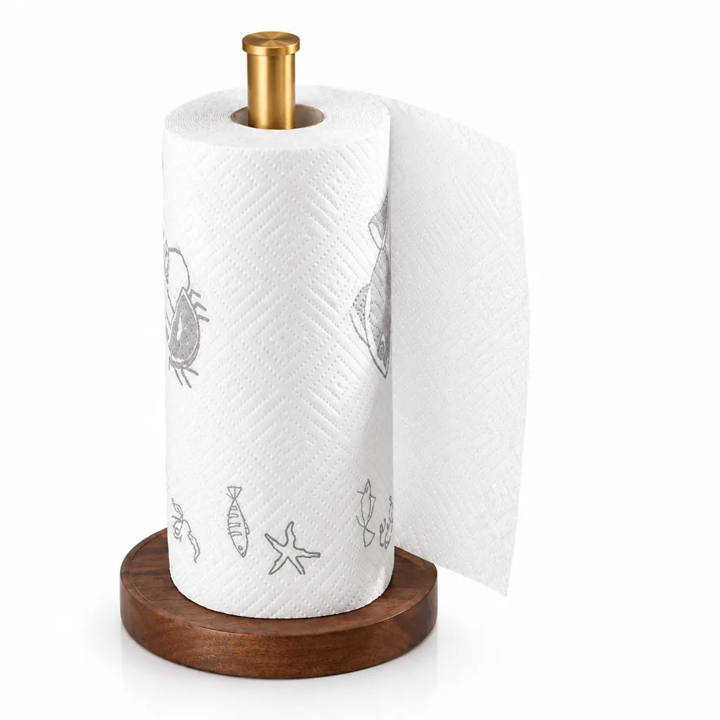 A roll of white kitchen paper printed with grey crab, fish and starfish motifs sits on the paper towel holder, which has a round walnut wood base and a slim brushed gold post, with a loose sheet hanging down one side against a plain white background.