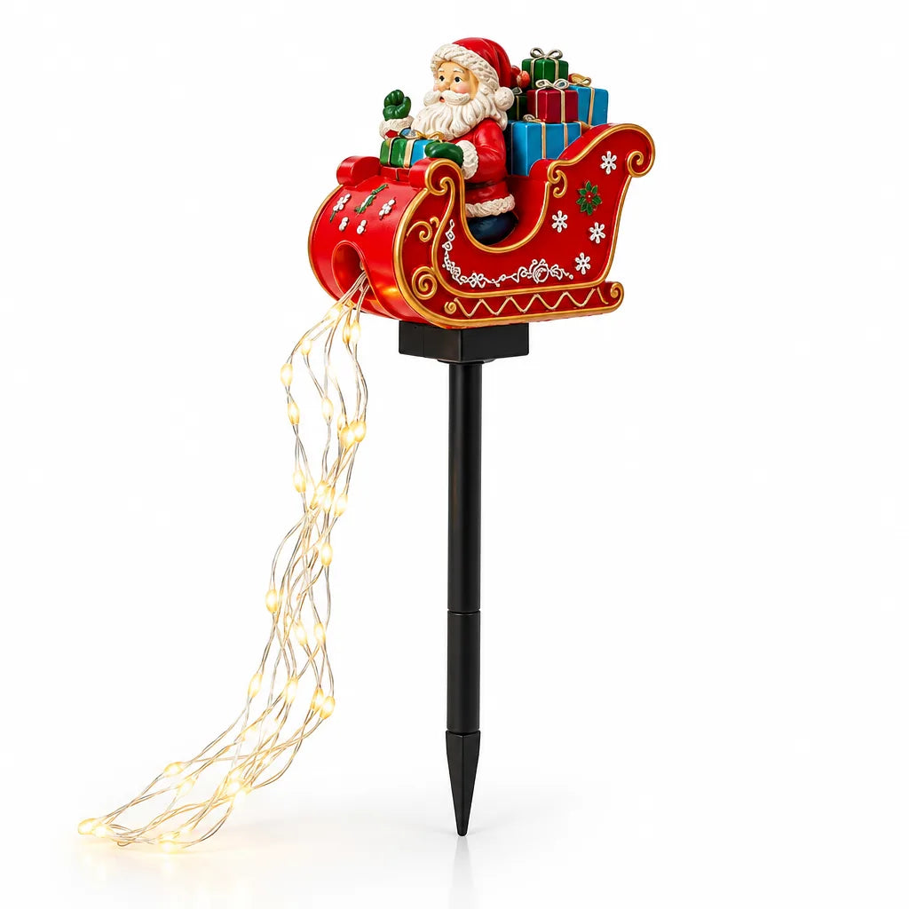 Solar garden stake shaped like a red sleigh with gold scrollwork, carrying a smiling Santa and a pile of wrapped gifts, mounted on a black pointed pole with a trailing strand of warm white LED lights spilling from the back onto a white background.