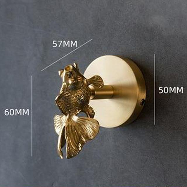 A gold-toned Solid Brass Animal Head Coat Hook shaped like a goldfish, mounted on a round base against a grey wall, with measurement lines marking 57MM, 60MM and 50MM.