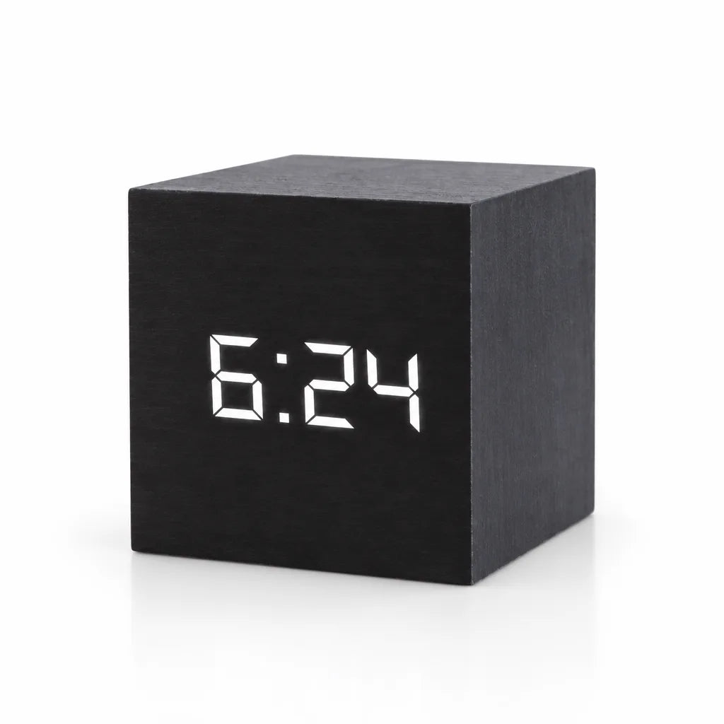 Black cube-shaped digital LED alarm clock with a wood-grain finish, showing the time 6:24 in white LED digits on its front face, against a plain white background.
