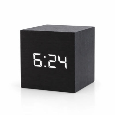 Black cube-shaped digital LED alarm clock with a wood-grain finish, showing the time 6:24 in white LED digits on its front face, against a plain white background.