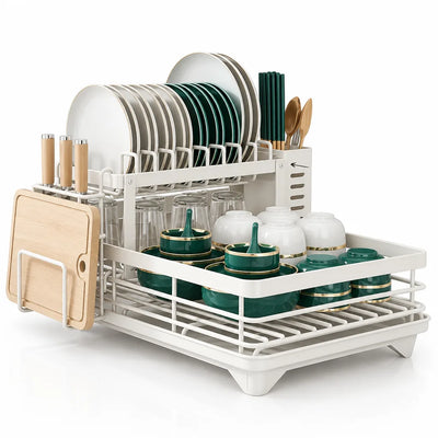 White two-tier dish drying rack holding plates, green and white bowls, glasses, chopsticks and wooden utensils, with a side knife block and a light wood cutting board clipped to the end.
