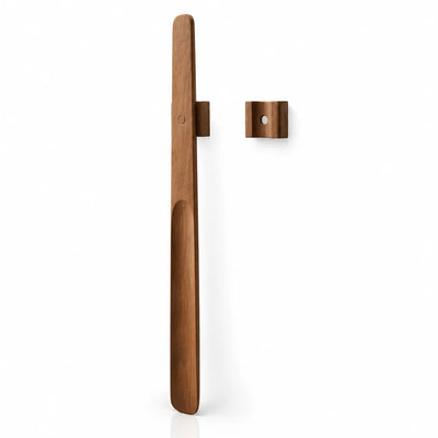 Extra-long walnut shoehorn in a vintage finish shown upright beside its small square magnetic wall mount against a white background.