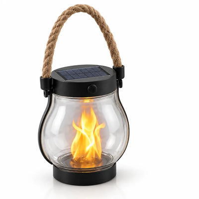 Solar flame lantern standing upright against a plain white background, its rounded clear glass globe glowing with an orange flickering flame effect, topped by a black lid with a small solar panel and push button, and carried by an arched braided rope handle.